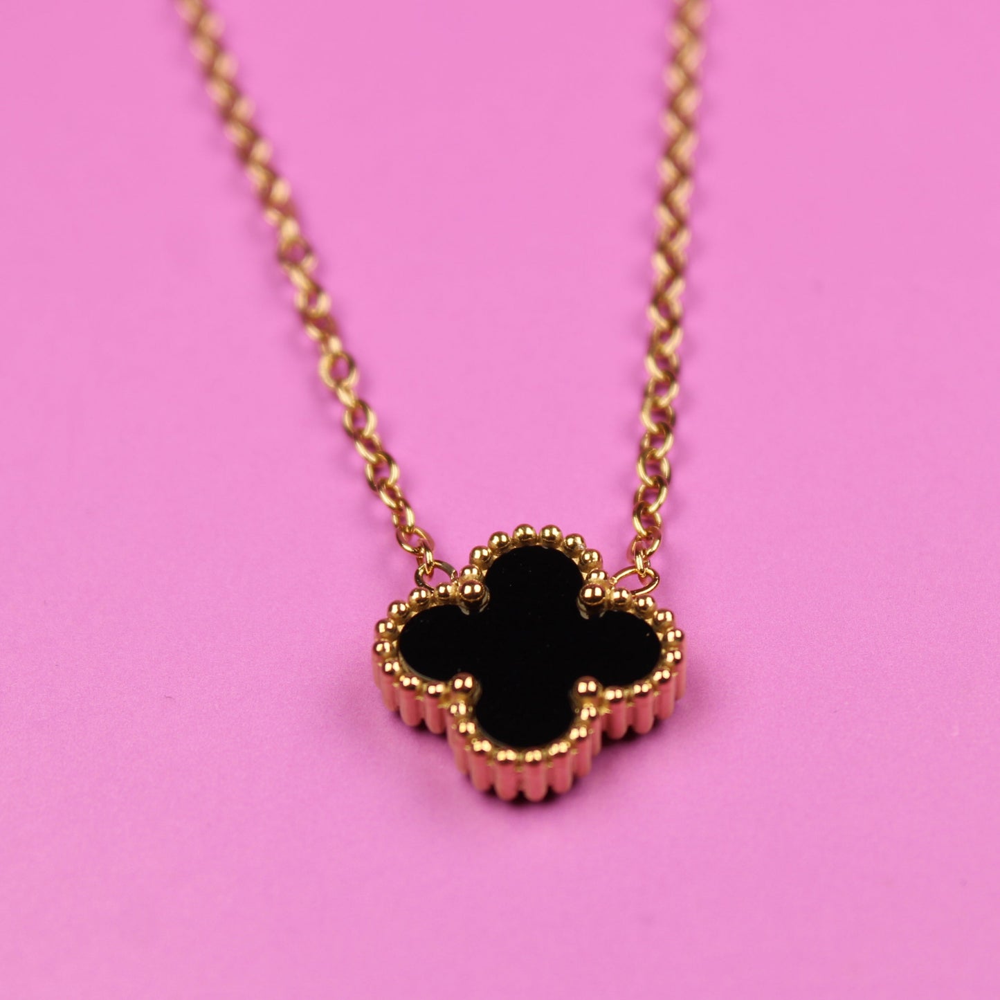 Necklace with a black clover pendant on a pink background