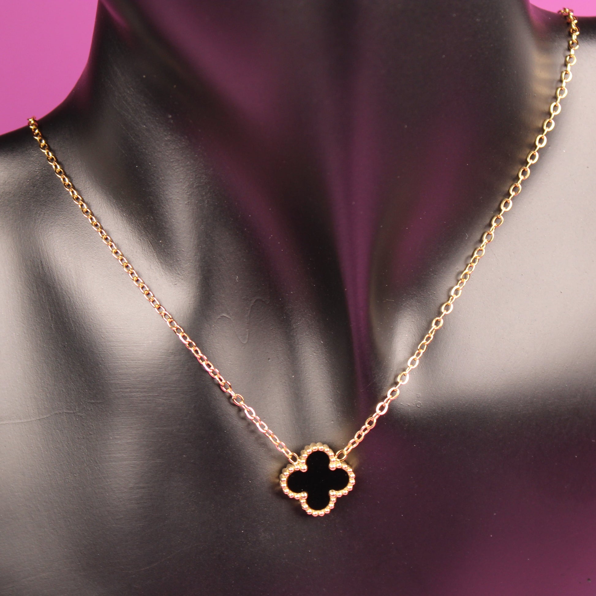 Gold necklace with a clover-shaped pendant on a mannequin bust against a pink background