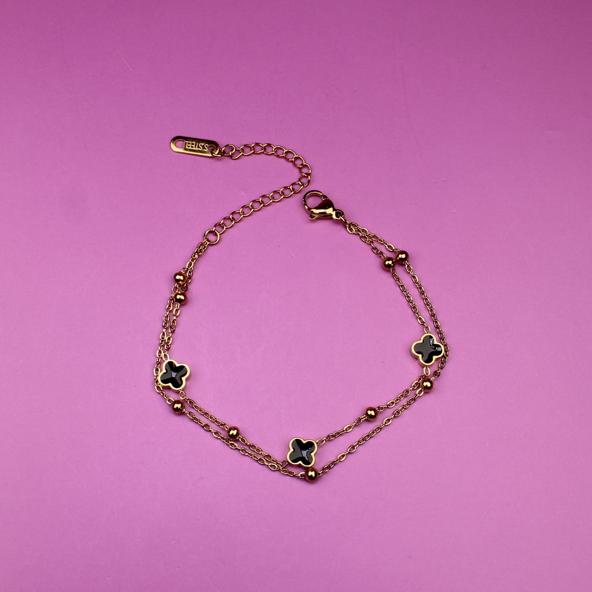 Gold bracelet with clover-shaped charms on a pink background